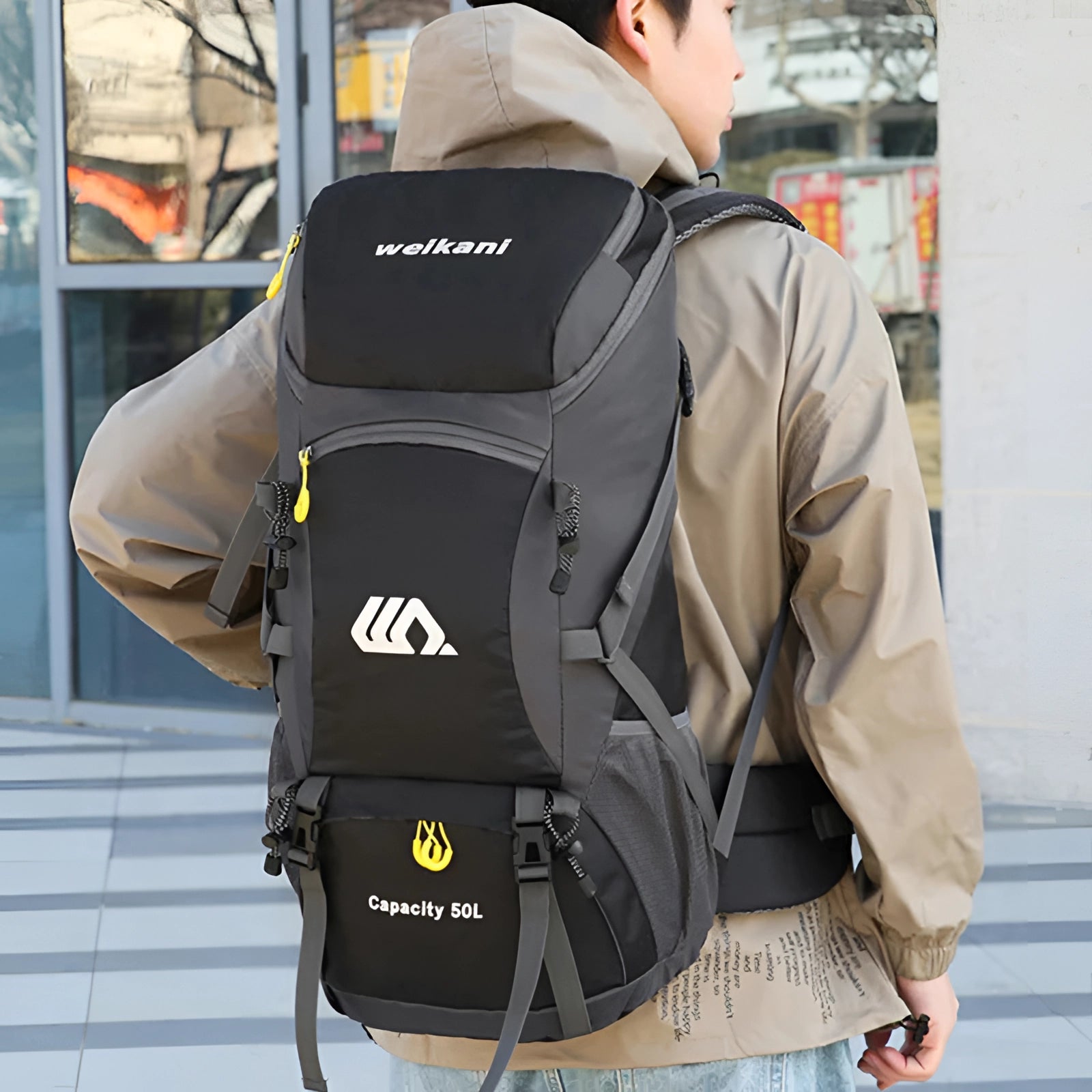 50-liter grey waterproof hiking backpack with back support and multiple compartments, featuring adjustable shoulder straps, displayed alongside a traveler wearing a baseball cap.