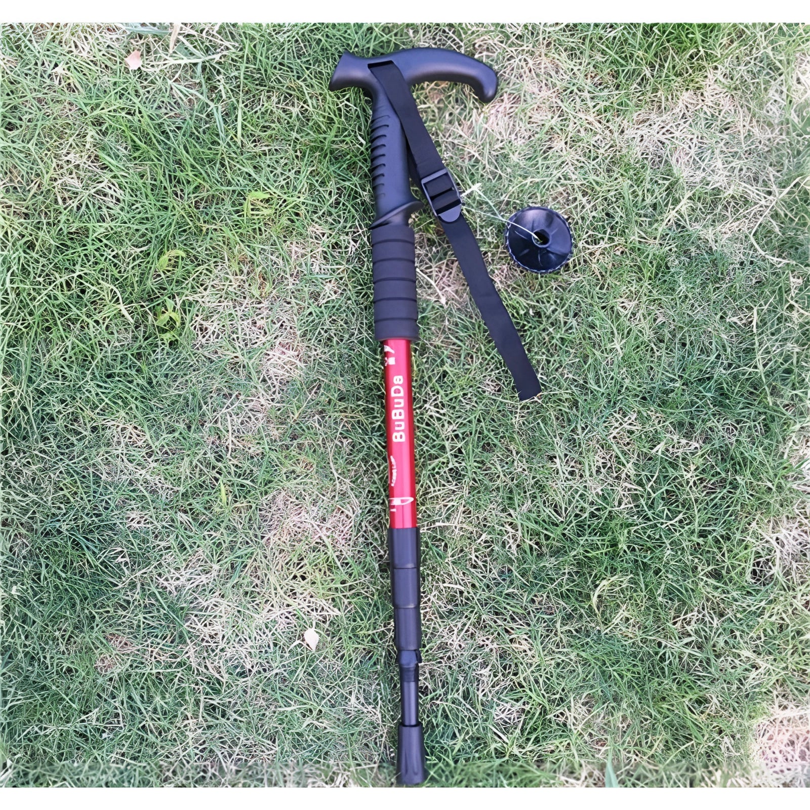 Red L-shaped adjustable trekking poles, lightweight and ergonomic with shock-absorbing technology, positioned on grass.