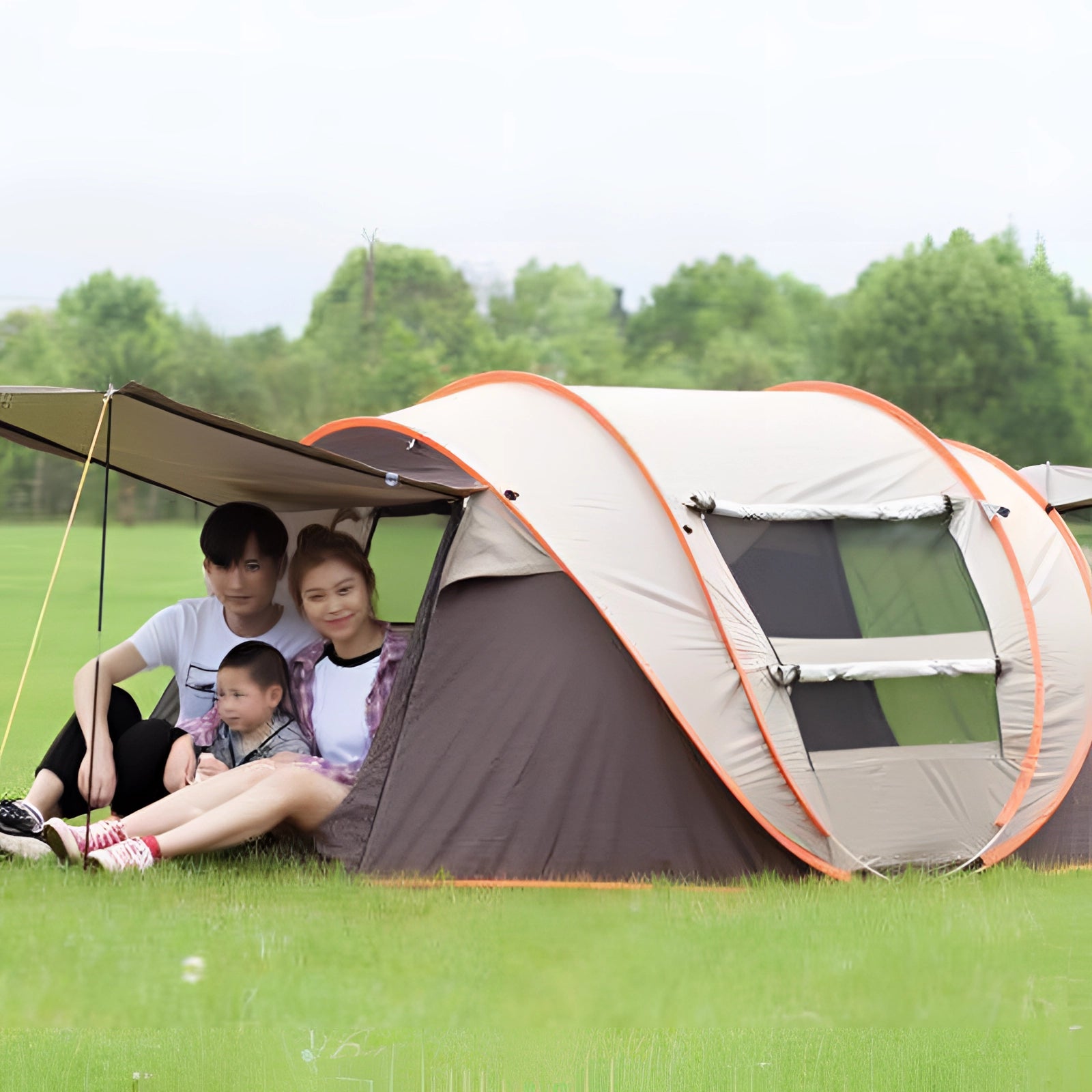 Automatic pop-up camping tent in brown color set up on a grassy field with trees and a clear sky in the background.