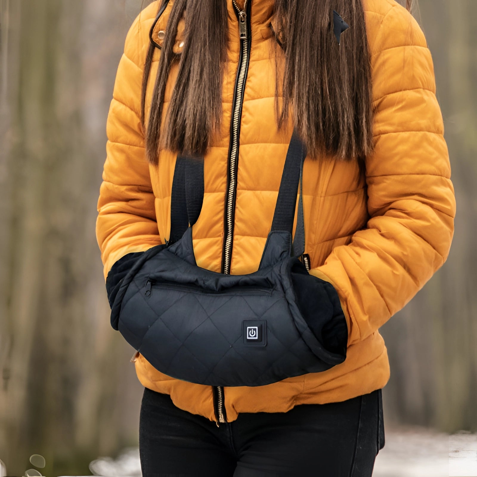 Black quilted handbag with USB charging port, adjustable strap, and mobile pocket, worn by a person in an orange jacket.