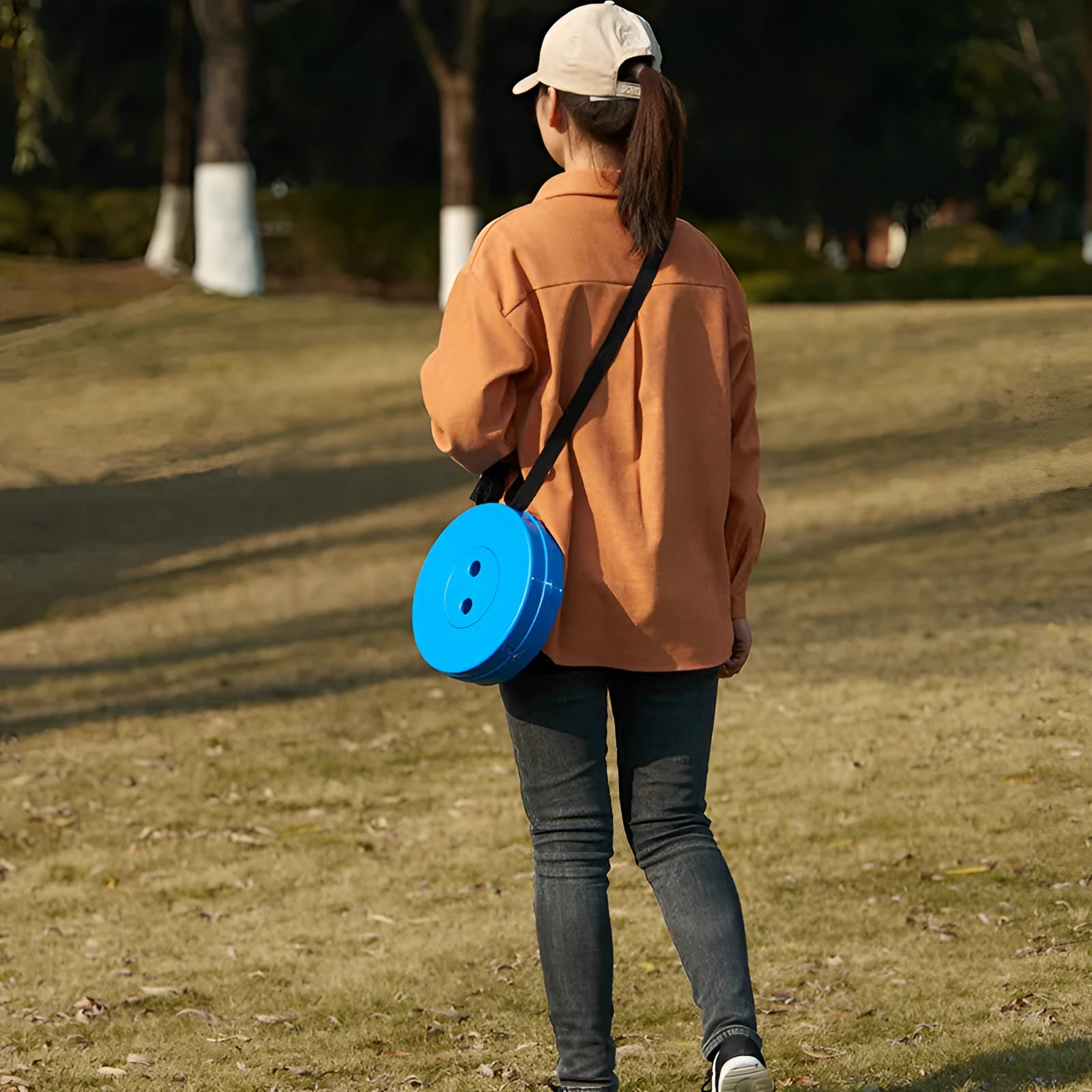 Collapsible telescopic camping stools set up in a grassy area with people enjoying leisure time in nature, surrounded by trees and wearing casual outdoor clothing and eyewear.