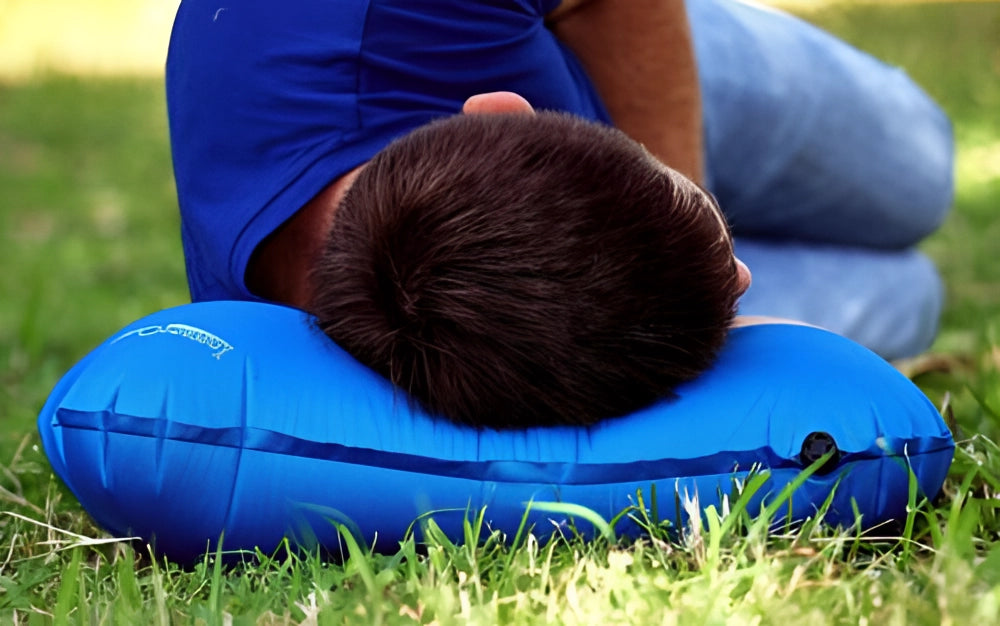 Compact lightweight blue inflatable camping pillow on grass, designed for easy inflation, portable and suitable for outdoor leisure and recreation.