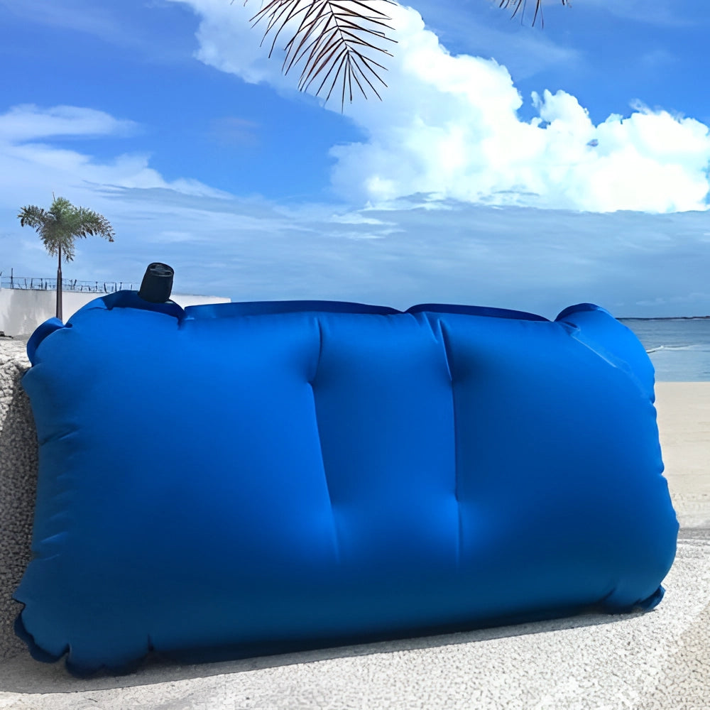 Compact lightweight inflatable blue camping pillow outdoors against a blue sky with trees in the background, highlighting its portability and comfort.