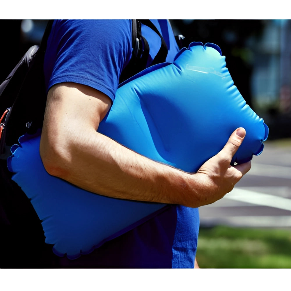 Blue compact lightweight inflatable camping pillow being held and inflated by a person's hand.