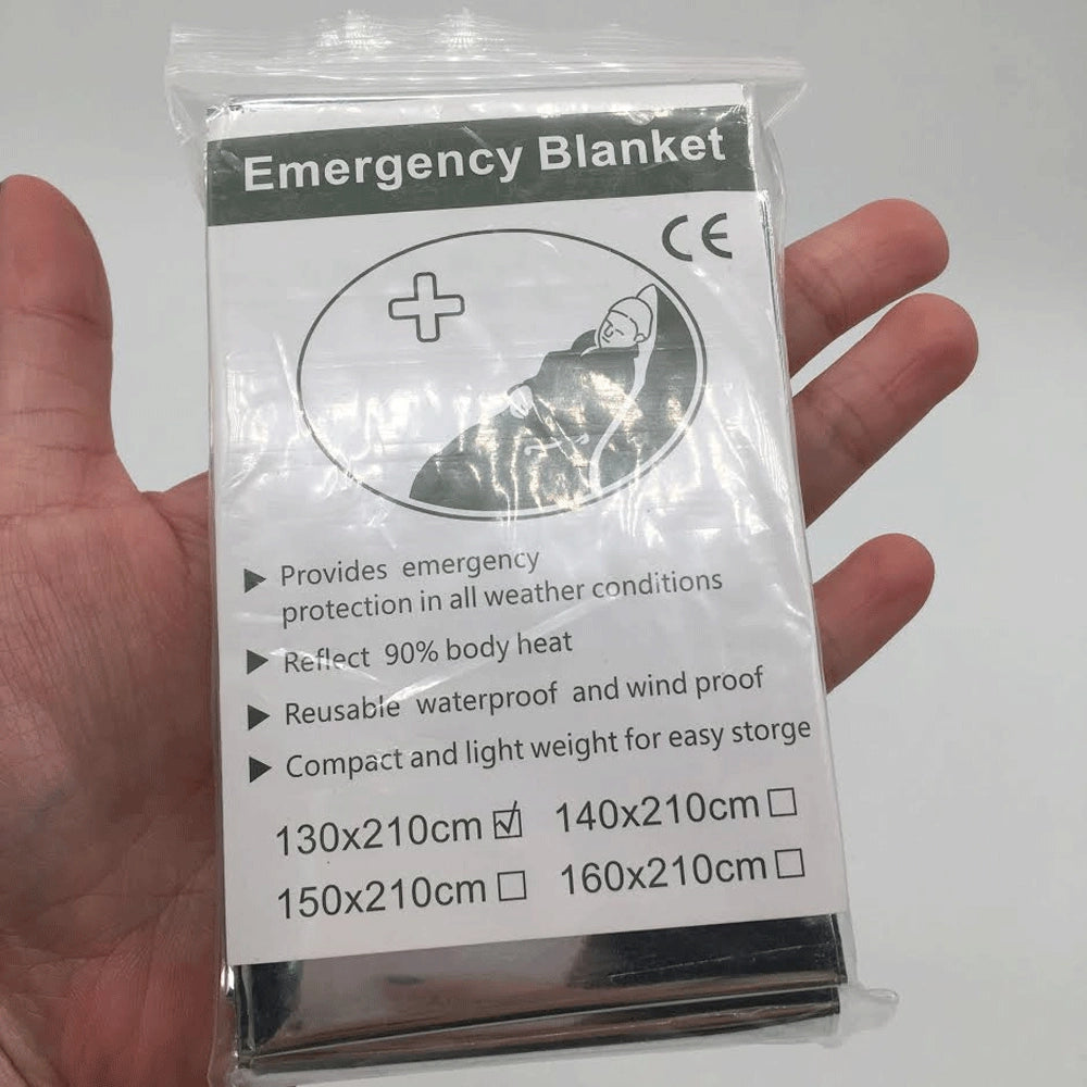 A hand holding a lightweight, reflective emergency thermal blanket made of heat-retaining mylar material.