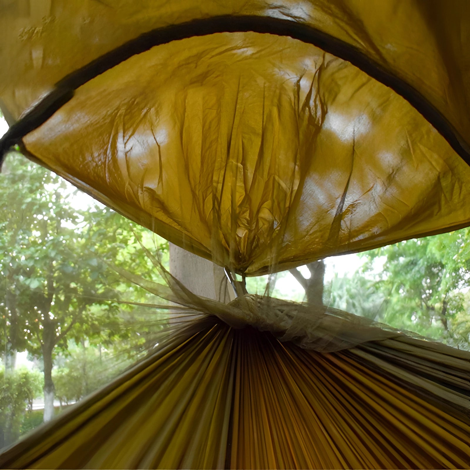 Enclosed mosquito-proof outdoor mesh hammock with dual-entry, set up in a shaded area among trees and nature with sunlight filtering through leaves.