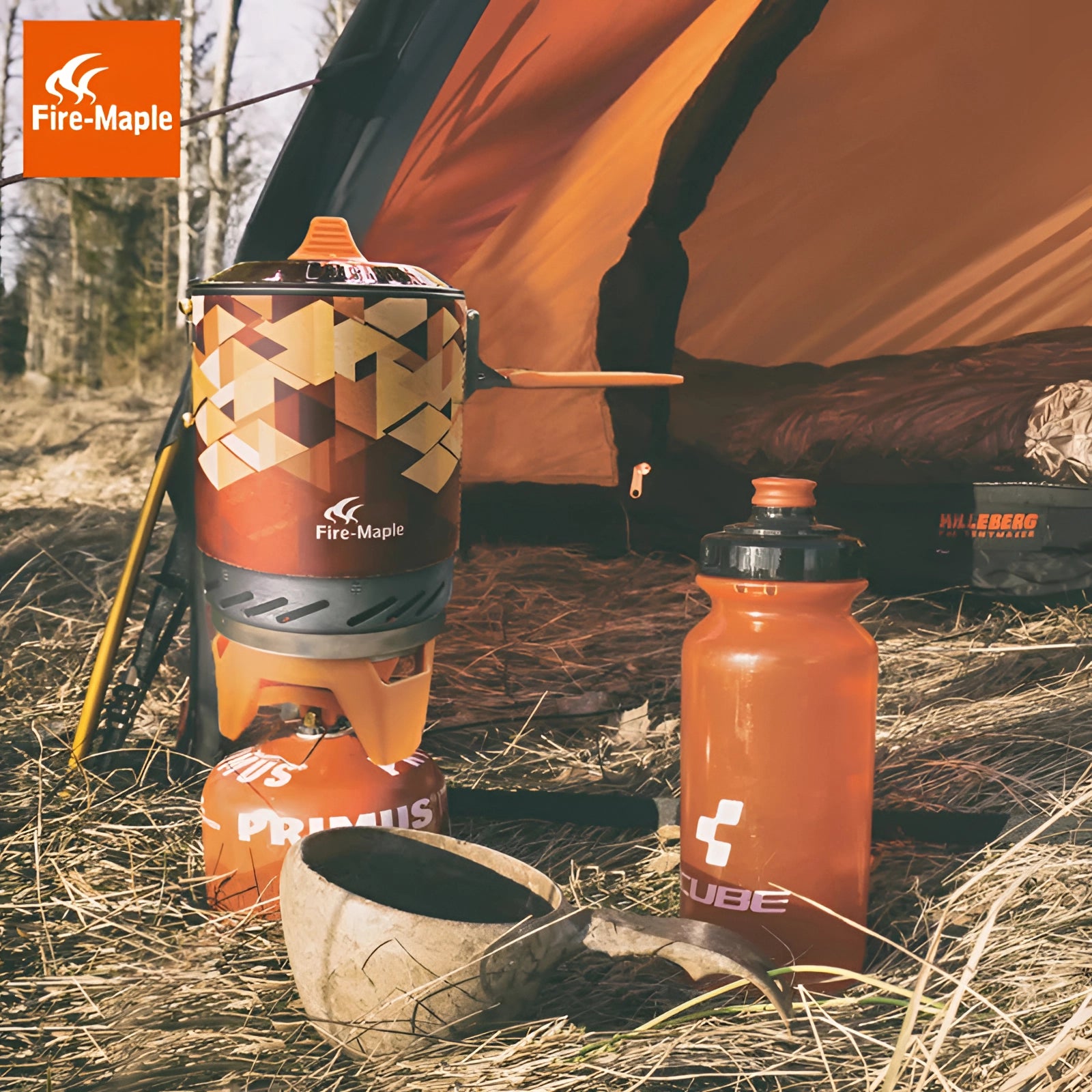 
An orange Fire-Maple X2 Compact Camping Stove set up outdoors, featuring a lightweight and windproof design with a plastic bottle nearby, situated on a natural landscape background.