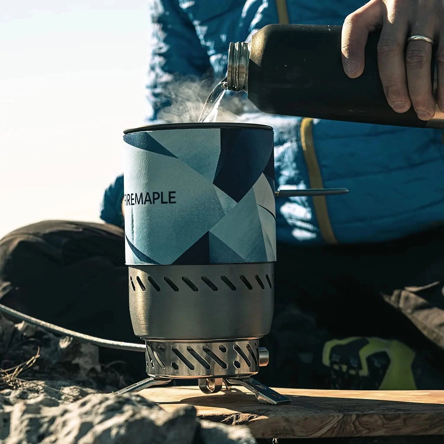 Compact, windproof camping stove with sleek electric blue finish, featuring a cylindrical design and glass components, ideal for outdoor cooking.