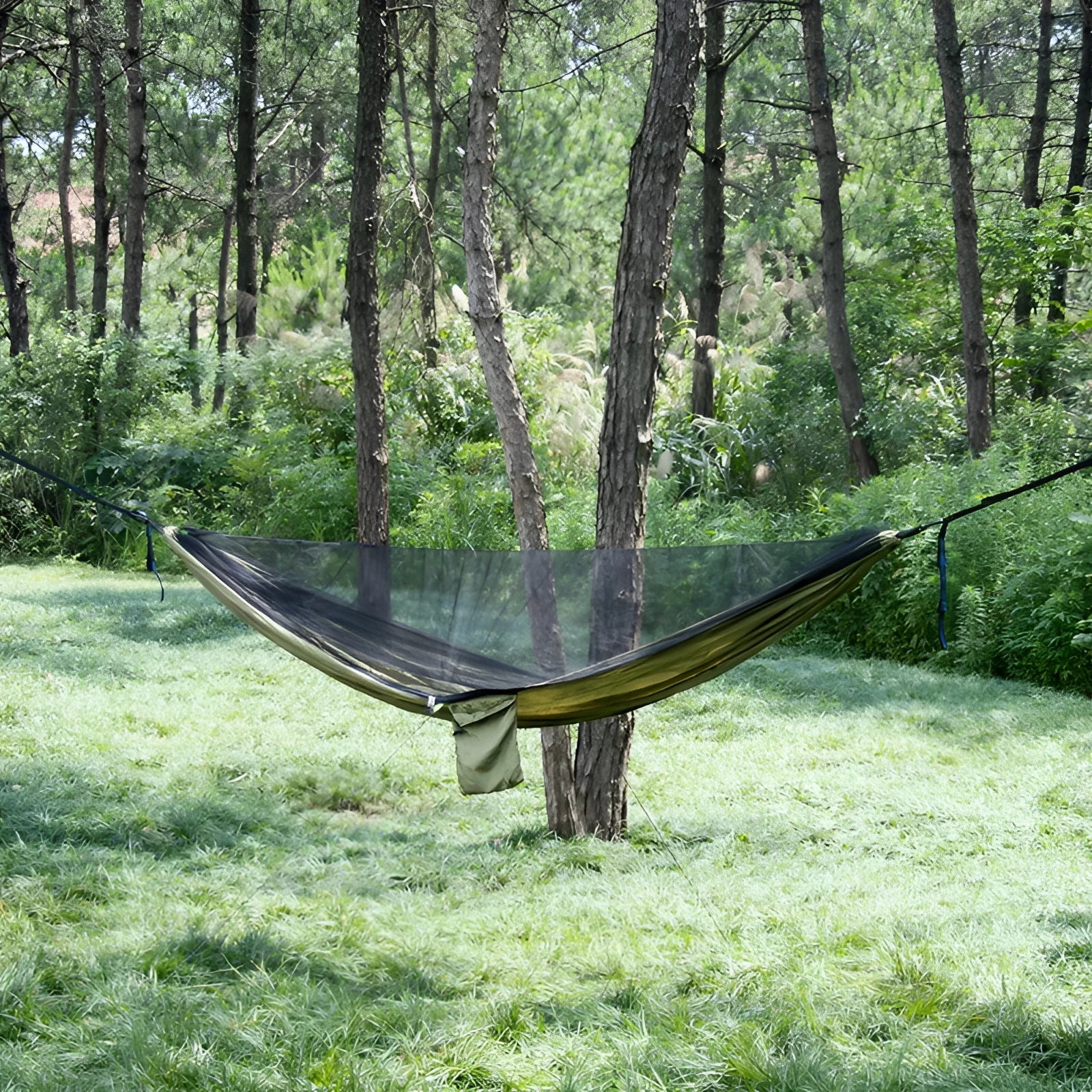 Green lightweight mosquito net hammock suspended between trees in a shaded natural landscape.