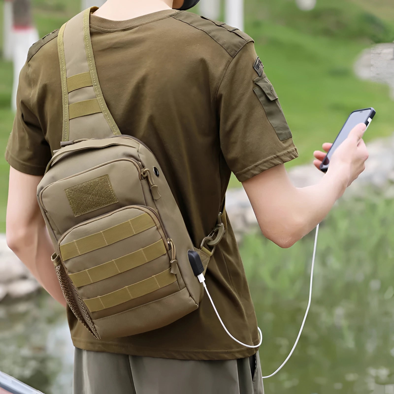 Khaki tactical sling bag with military-style camouflage design, featuring a USB port and water-resistant material, shown being held by a hand.