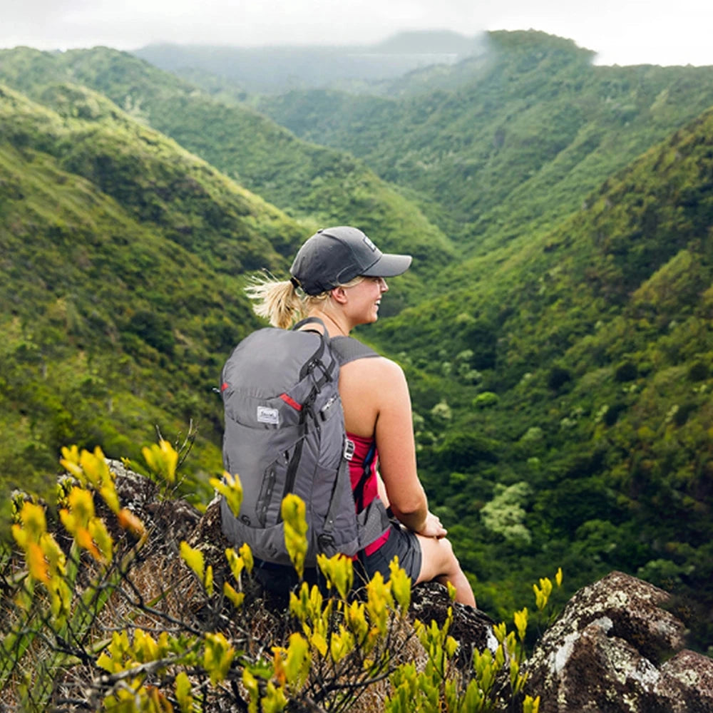 Lightweight water-resistant Scione backpack set against a scenic backdrop of lush green plants and mountain landscape, capturing the essence of travel and adventure in nature.