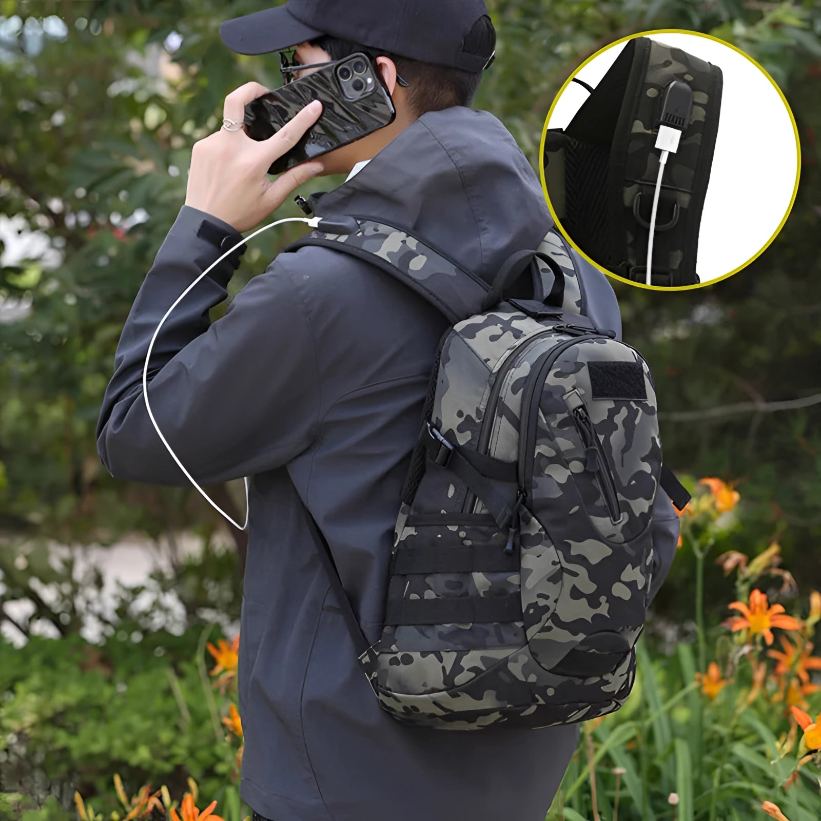 Durable outdoor military-grade tactical backpack in a natural setting with greenery, equipped with a USB charger, photographed alongside camera gear and a baseball cap.