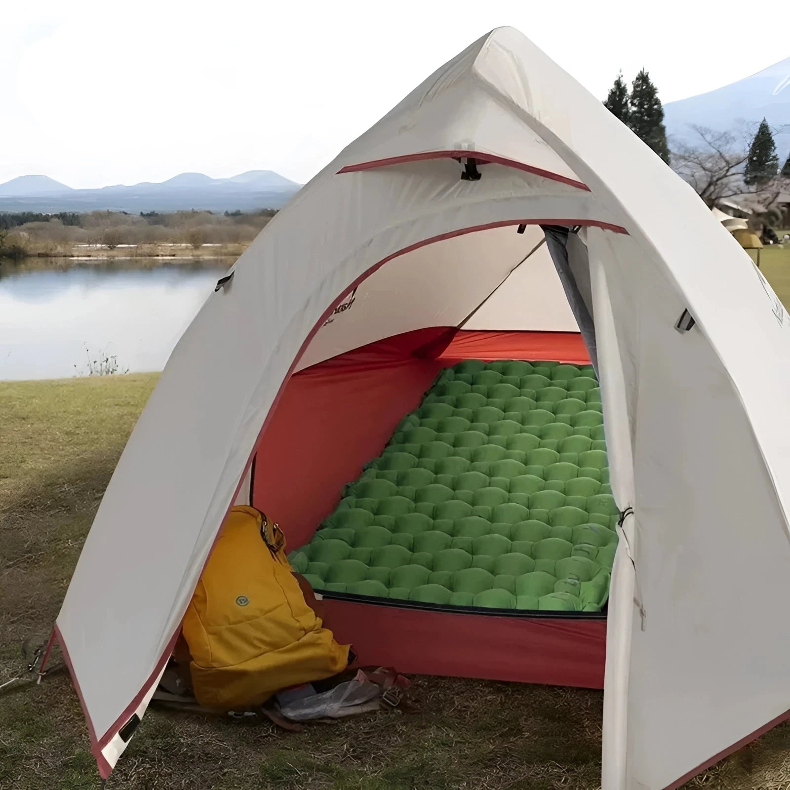 Naturehike ultralight inflatable camping sleeping pad set up inside a tent in a grassy area with trees and a clear sky in the background.