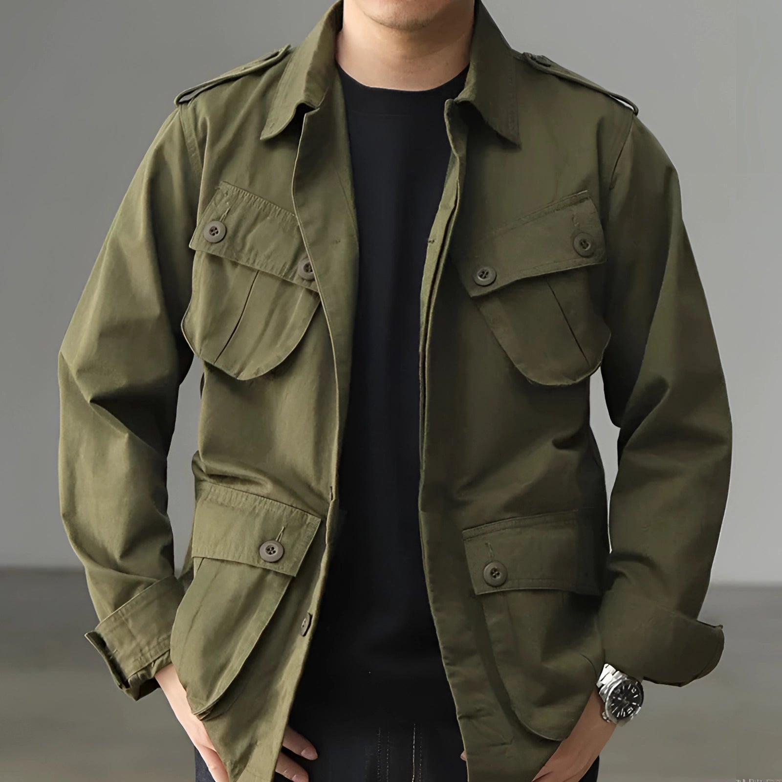 Men's green tactical military utility jacket worn outdoors, featuring a high collar and multiple pockets, with buttoned cuffs on the sleeves.