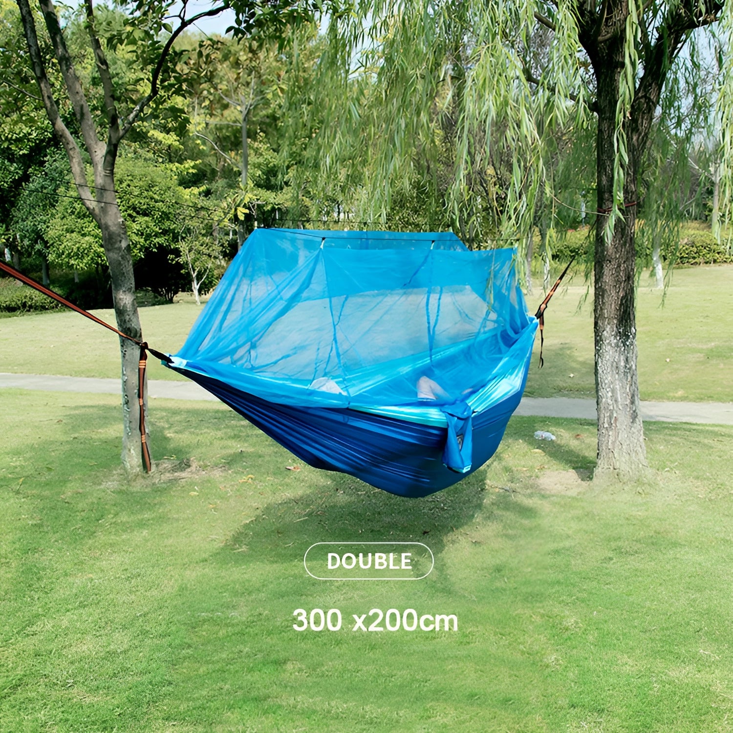 Portable double nylon camping hammock with mosquito net and tree straps set up between trees in a grassy, shaded area.