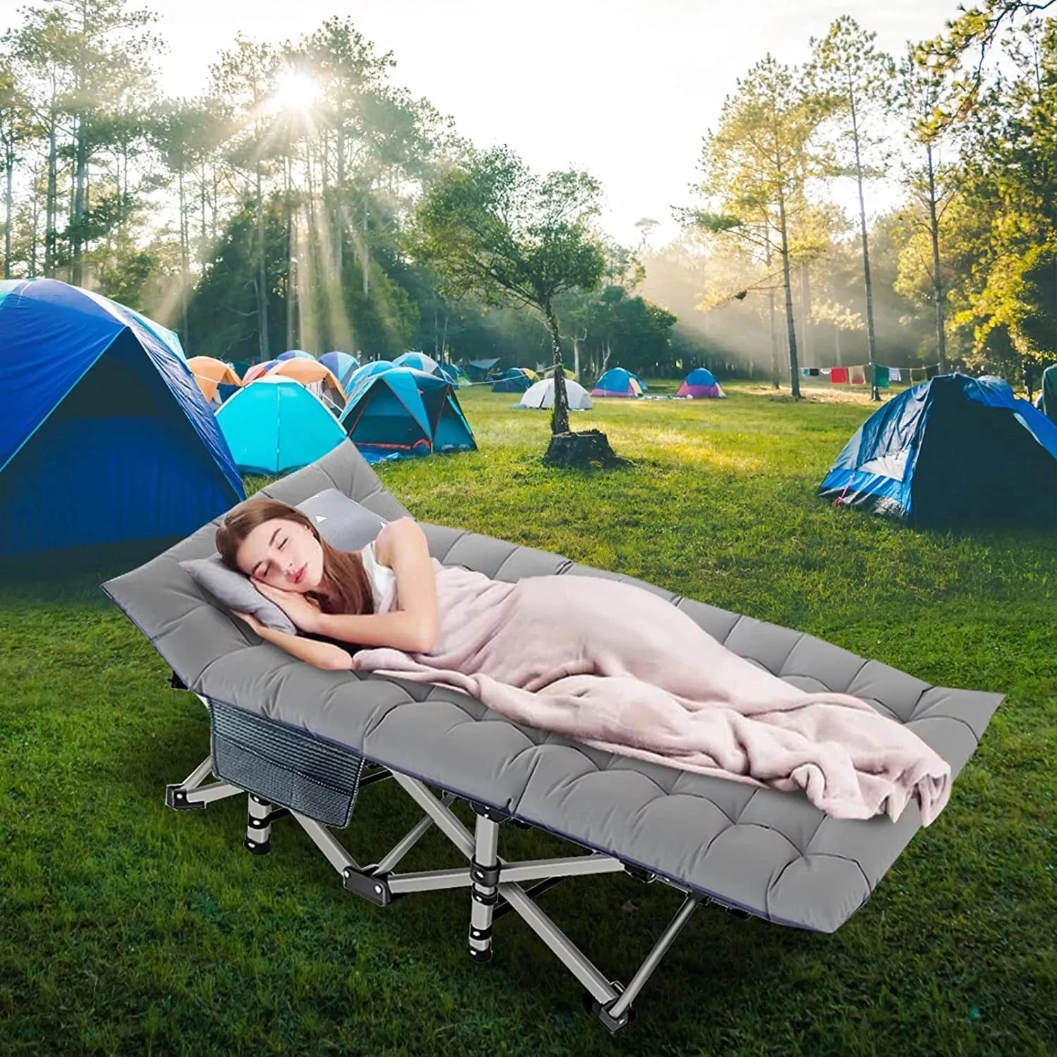 Portable lightweight folding camping cot set up on grass under a tent with trees and blue sky in the background, providing comfort and shade for leisure activities.