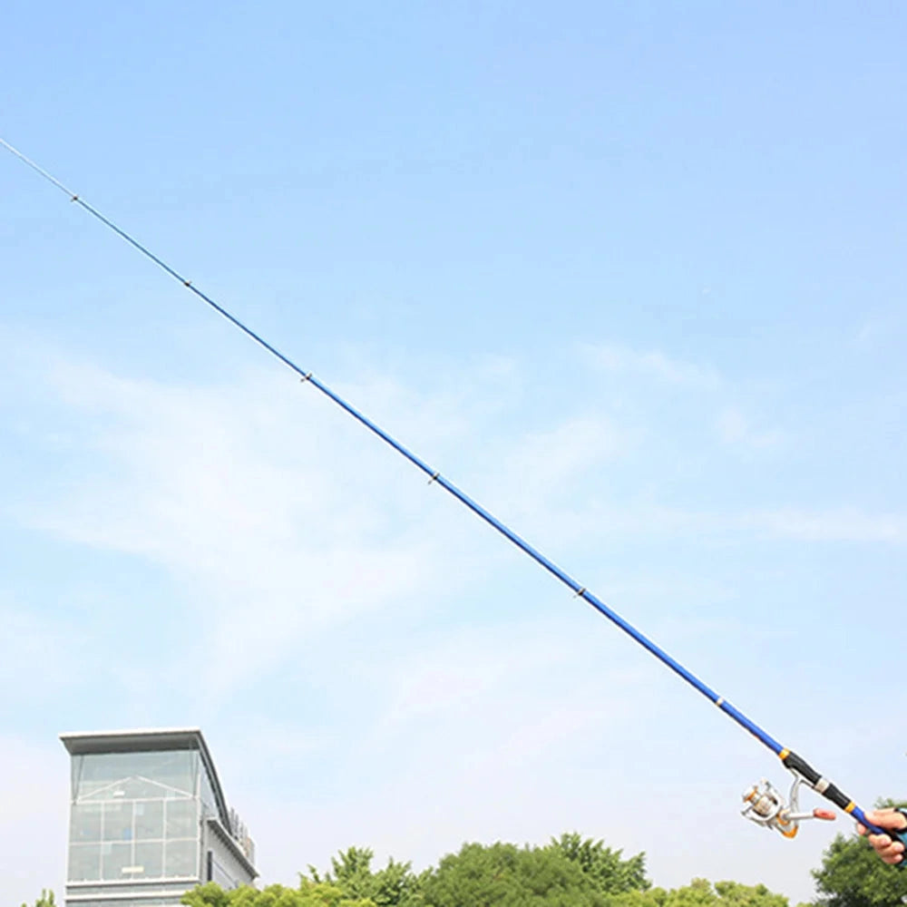 Telescopic fishing rod and reel combo set up in a grassy outdoor setting with a clear sky and cumulus clouds in the background, power lines and buildings visible.