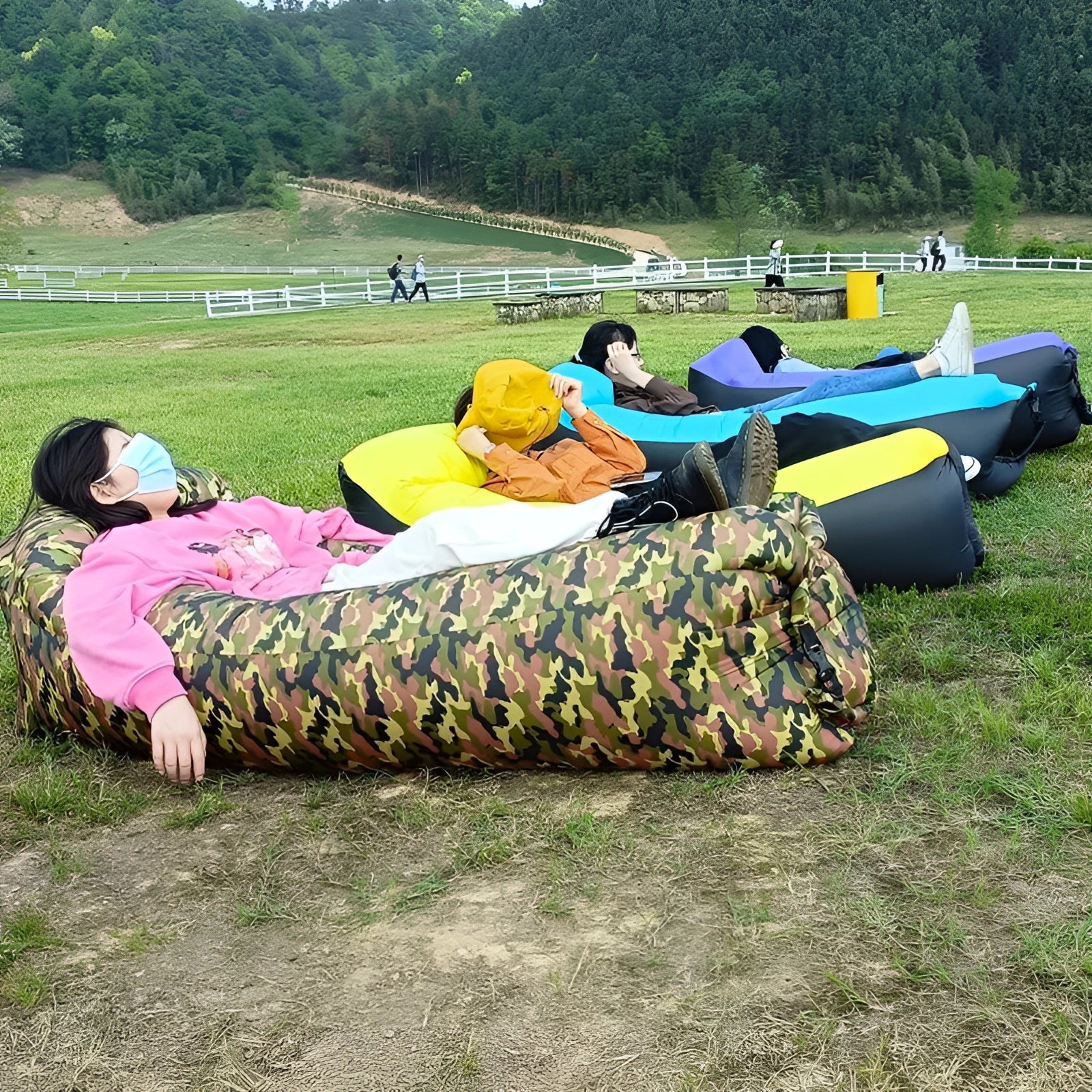 People relaxing on a waterproof outdoor inflatable sofa in a grassy natural environment with trees and other plants in the background.