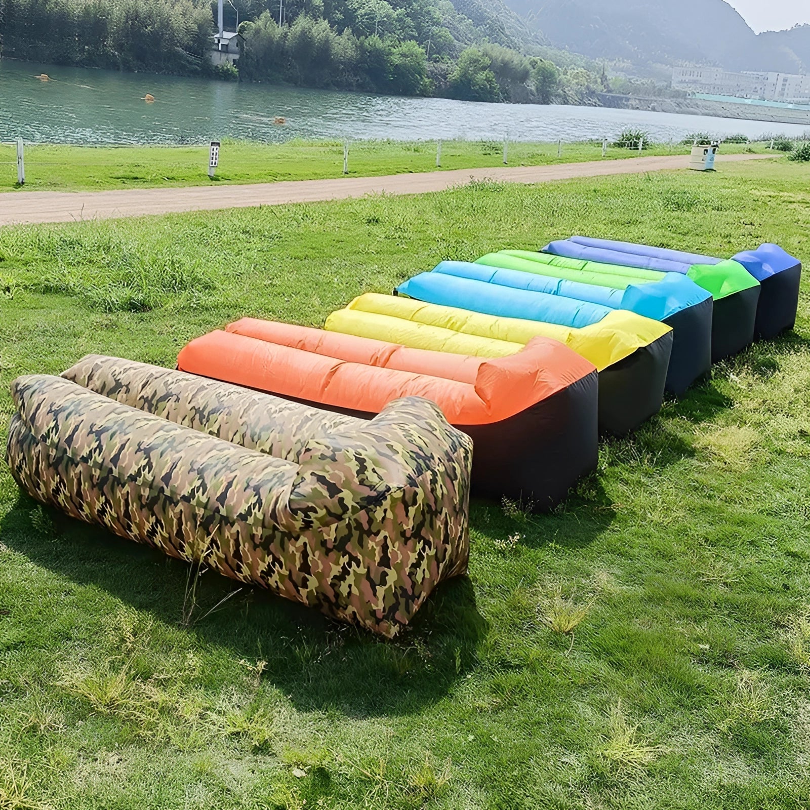 Waterproof outdoor inflatable sofa set up on a grassy field near a body of water with trees and a clear sky in the background.