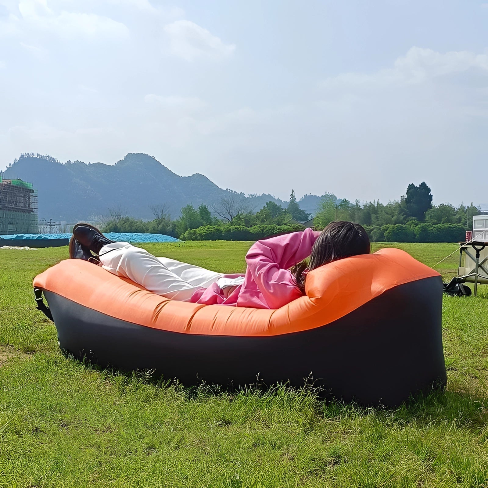 Waterproof outdoor inflatable sofa set up on a grassy field with clear skies and scattered clouds in the background, surrounded by trees and open landscape.