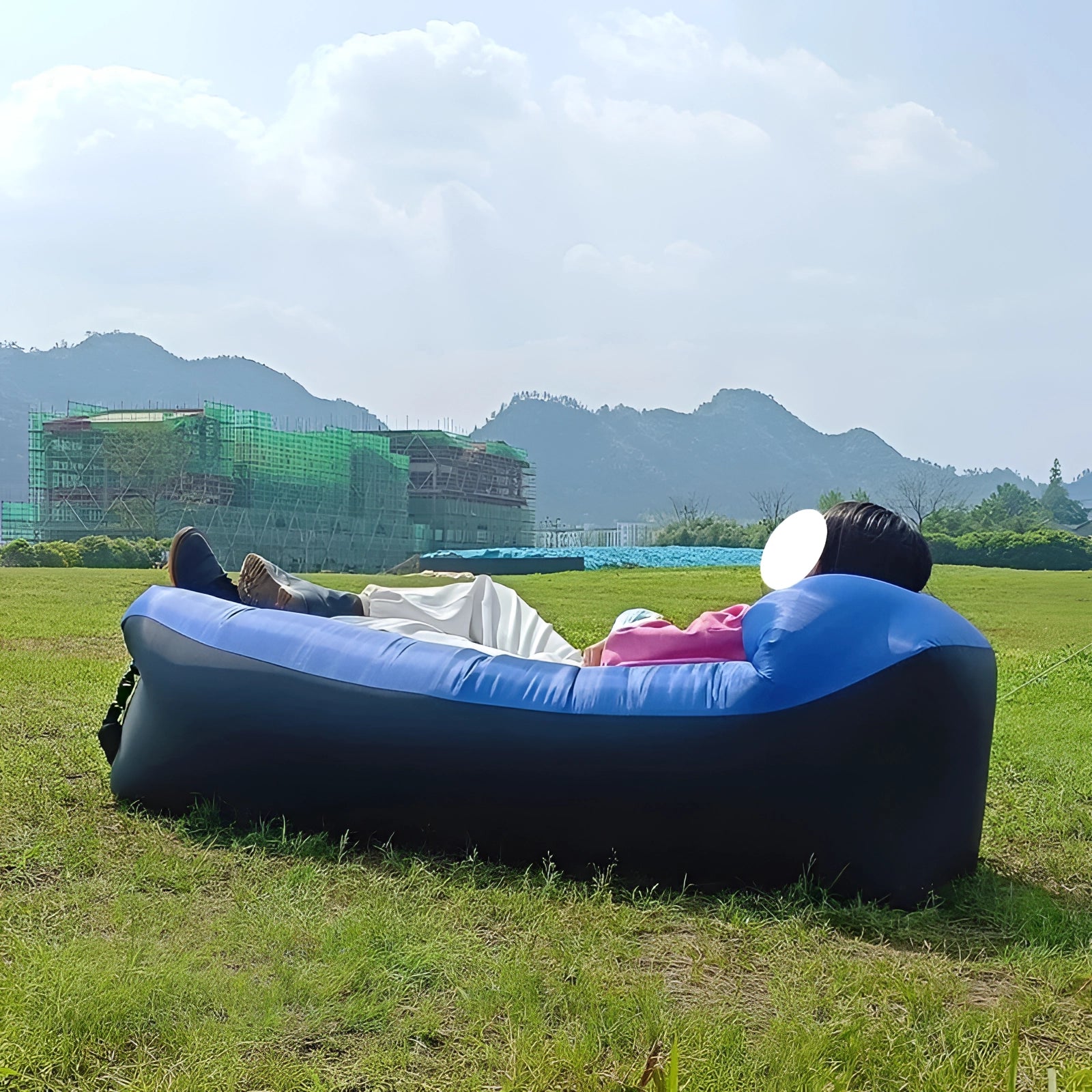 Blue Waterproof Outdoor Inflatable Sofa set up on a grassy field with a backdrop of a clear sky and distant mountains.