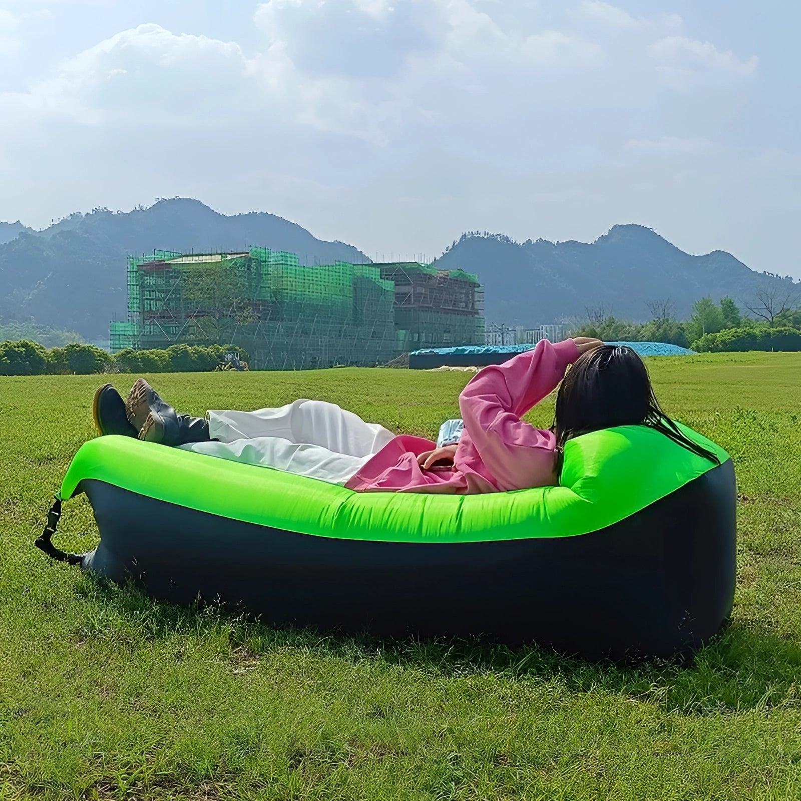 Green Waterproof Outdoor Inflatable Sofa set up on a grassy field with a clear sky and mountains in the background, showcasing a comfortable and fun leisure product.