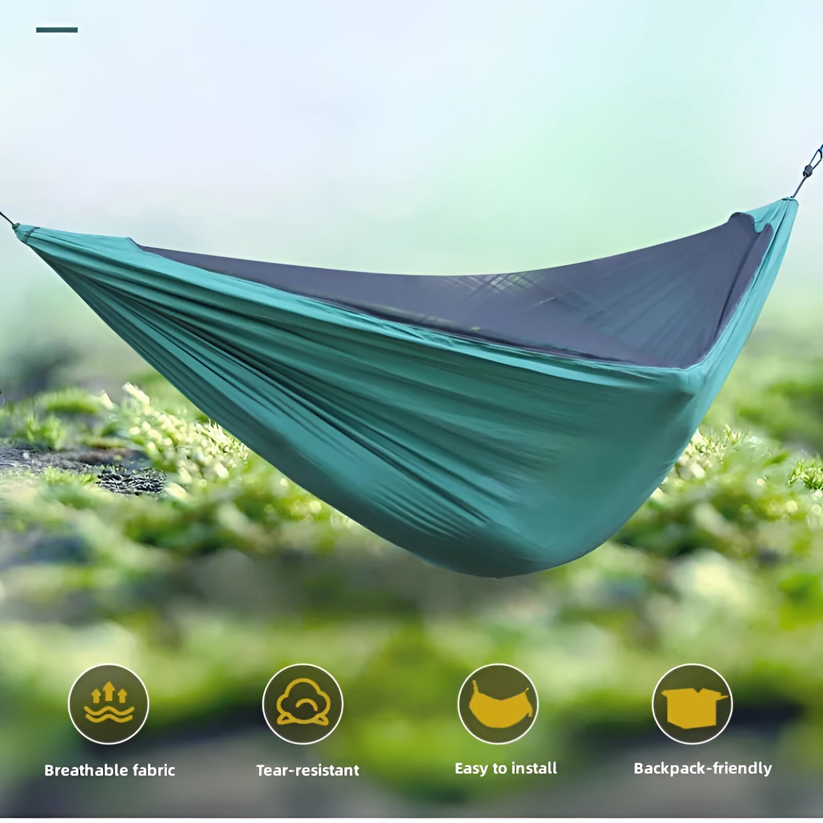 Waterproof portable camping hammock set up between trees in a grassy area with a clear sky in the background and natural landscape.