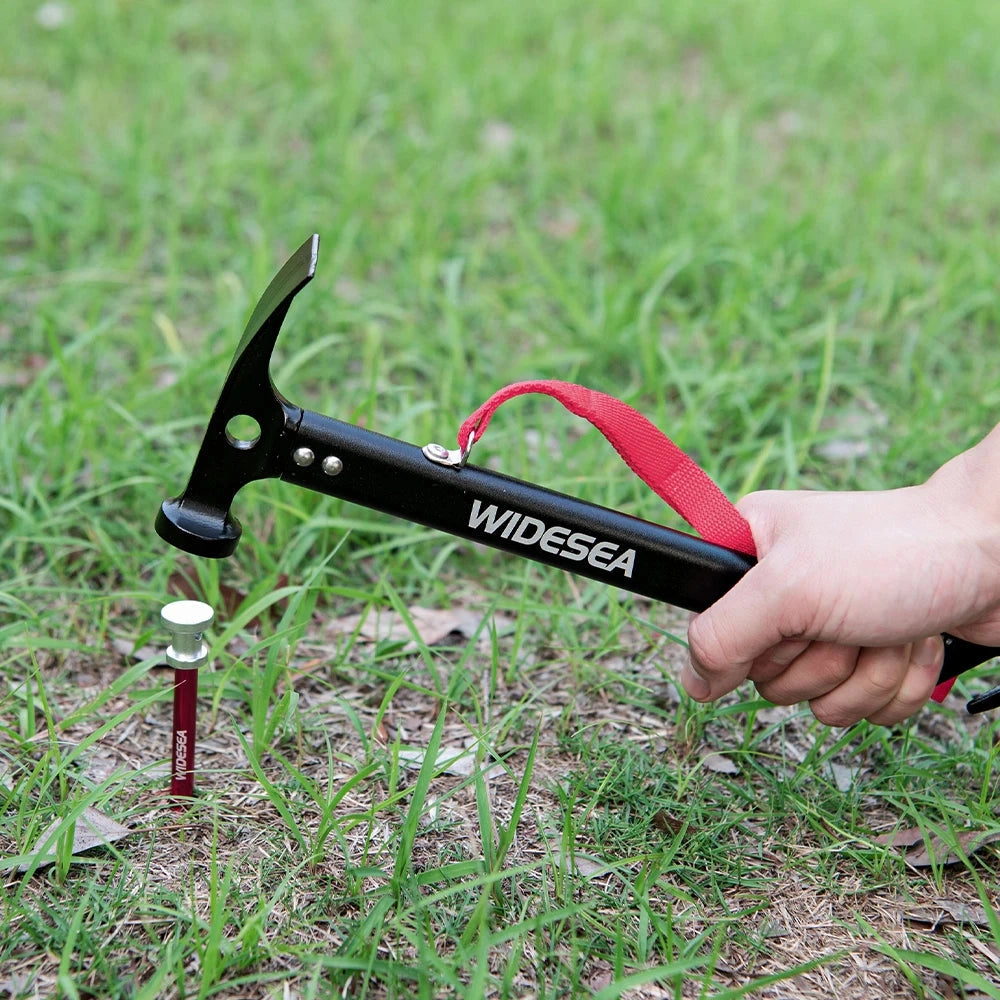 Aluminum camping hammer with tent stake puller resting on grass.