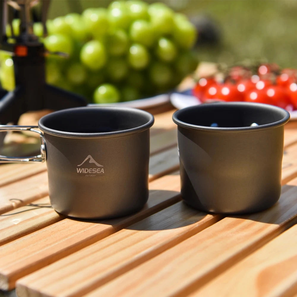 Titanium camping mug on a wooden table surrounded by tableware and plants.