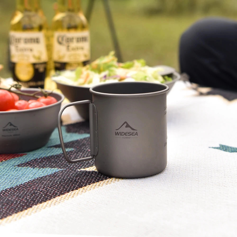 WideSea Titanium Camping Mug & Cookware Set featuring a lightweight and portable titanium mug alongside cooking utensils; the set is displayed with fresh ingredients such as plum tomatoes, emphasizing its use in outdoor cooking and meal preparation.