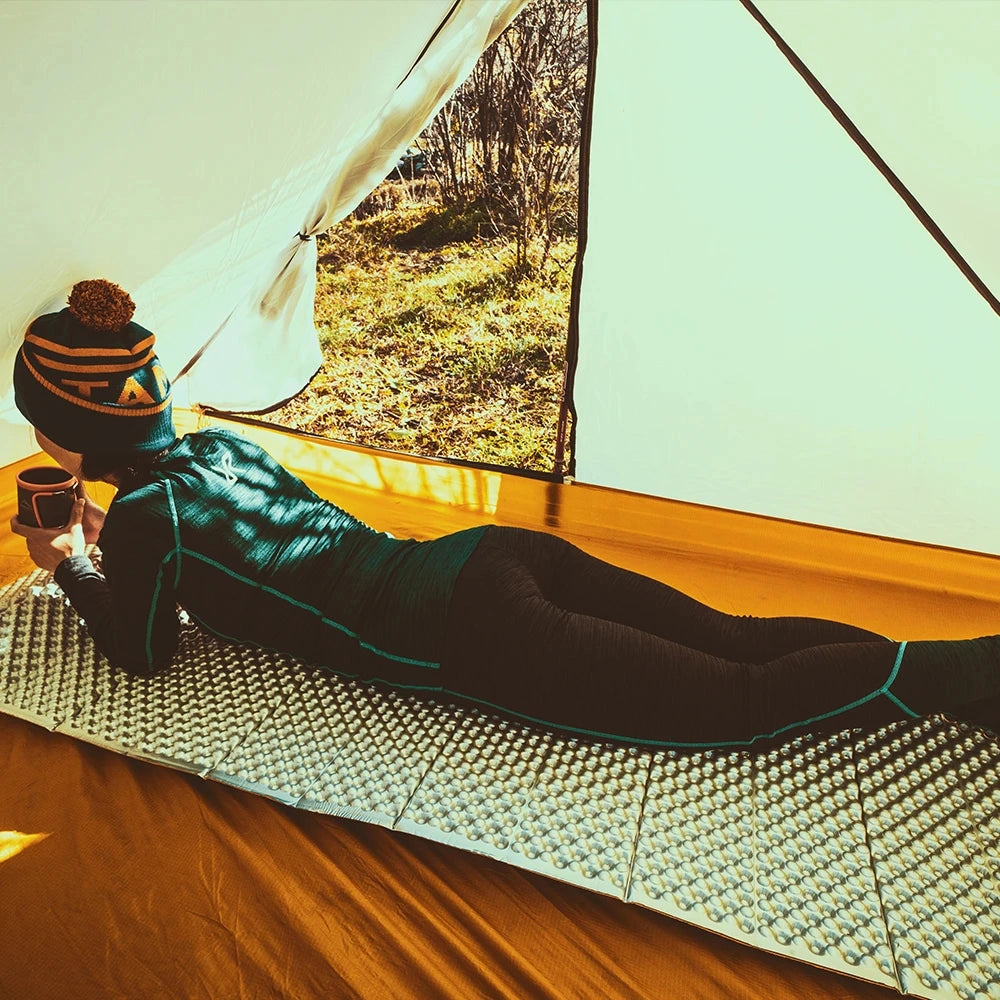 Ultralight camping mat laid out on a lightly shaded, natural wooden surface, showcasing its compact and non-slip features.